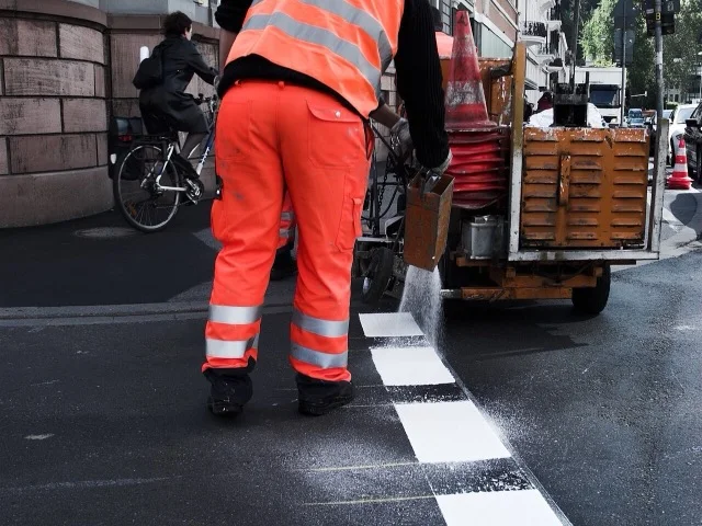 Láthatósági ruhás dolgozó biztonsági jelölést helyez el a munkaterület határán
